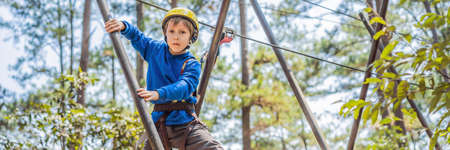 BANNER, LONG FORMAT Happy child in a helmet, healthy teenager school boy enjoying activity in a climbing adventure park on a summer dayの写真素材