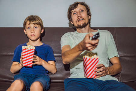 Father and son watching TV and eat popcort in evening at homeの写真素材