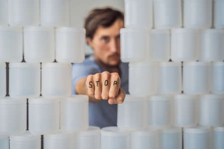 Man showing stop surrounded by many jars of yoghurt that he uses in a year. A huge amount of plastic food jars. Excessive consumption of plastic. Reduce, reuse, recycleの写真素材