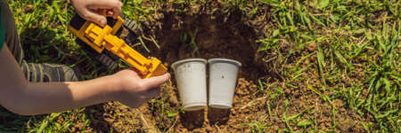 The boy plays recycling. He buries plastic disposable dishes and biodegradable dishes BANNER, LONG FORMATの写真素材