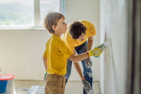 Man with his son makes repairs at home, he teaches children to plaster the walls with a spatula in his handsの写真素材