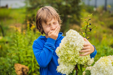 Little boy is blowing his nose on green meadow near flowers. Flower allergy conceptの写真素材