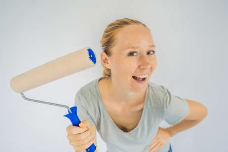 Woman house painter worker painting and priming wall with painting roller. DIY