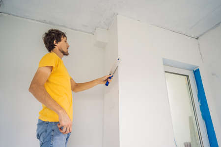 One male house painter worker painting and priming wall with painting roller. DIY