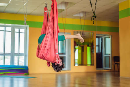 Senior mature woman practices anti-gravity yoga with a hammock in a studio. Lifestyleの写真素材