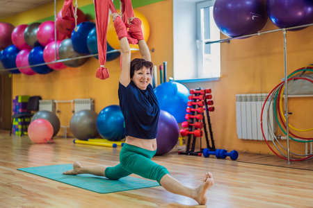 Senior mature woman practices anti-gravity yoga with a hammock in a studio. Lifestyleの写真素材