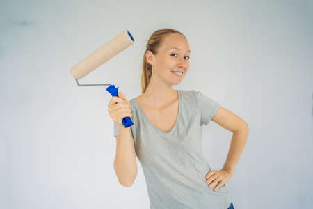 Woman house painter worker painting and priming wall with painting roller. DIY
