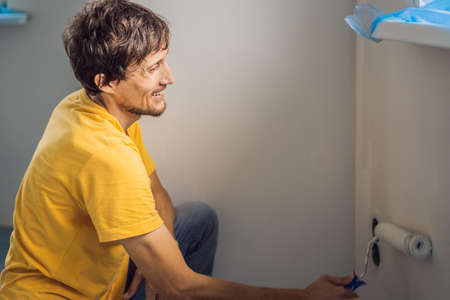 One male house painter worker painting and priming wall with painting roller. DIY