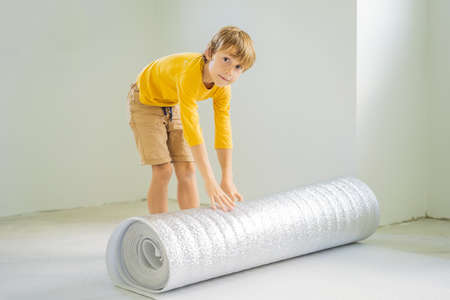 Boy are laying floor insulation. Roll of insulating cloth to install a laminate wooden floorの写真素材