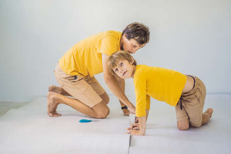 Dad and son are laying floor insulation. Roll of insulating cloth to install a laminate wooden floor