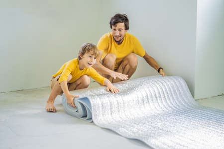 Dad and son are laying floor insulation. Roll of insulating cloth to install a laminate wooden floorの写真素材