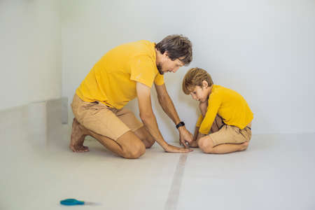 Dad and son are laying floor insulation. Roll of insulating cloth to install a laminate wooden floorの写真素材