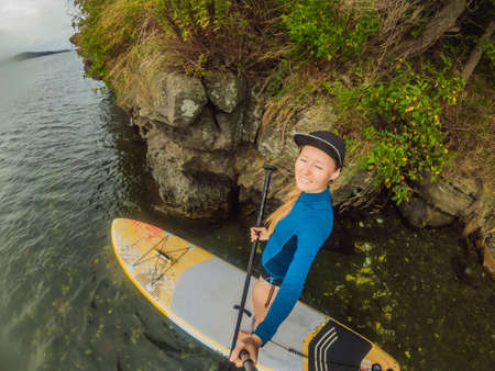 Young women Having Fun Stand Up Paddling in the sea. SUP. Red hair girl Training on Paddle Board...