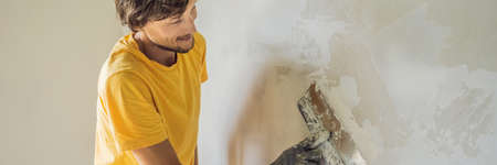 Plasterer home improvement handyman worker with putty knife working on apartment wall fillingの写真素材