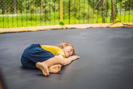 Happy boy plays outdoors in garden jumping high in the sky on trampolineの写真素材