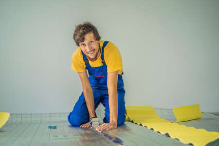 Master installs the overlapping thermal insulation in the room. Floor heating installation. Male hand holds reinforced tape. Repair in the apartment, floor insulationの写真素材