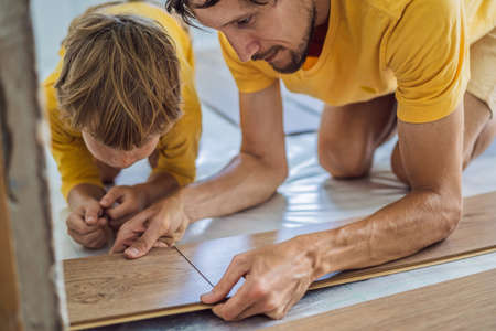 Father and son installing new wooden laminate flooring on a warm film floor. Infrared floor heating system under laminate floorの写真素材