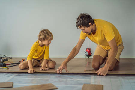 Father and son installing new wooden laminate flooring on a warm film floor. Infrared floor heating system under laminate floorの写真素材