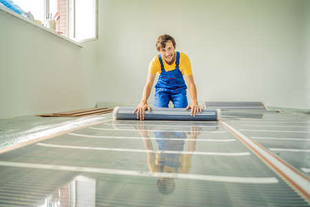 Master installs film warm floor in the room. Floor heating installationの写真素材