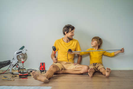 Father and son installing new wooden laminate flooring on a warm film floor. Infrared floor heating system under laminate floorの写真素材