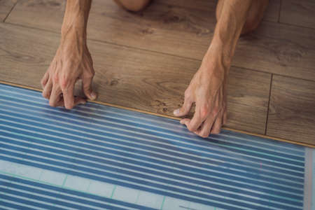 Man installing new wooden laminate flooring on a warm film floor. Infrared floor heating system...