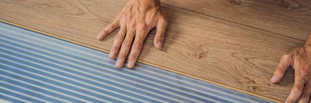 BANNER, LONG FORMAT Man installing new wooden laminate flooring on a warm film floor. Infrared floor...