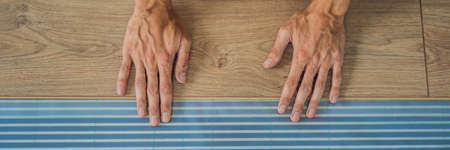 BANNER, LONG FORMAT Man installing new wooden laminate flooring on a warm film floor. Infrared floor heating system under laminate floorの写真素材