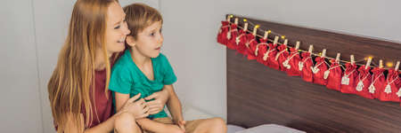 BANNER, LONG FORMAT Smiling boy sitting on a bed opening first present from advent calendar. Winter seasonal tradition. Copy spaceの写真素材