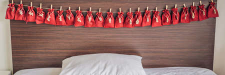 Advent calendar red bags on a rope hang on a childs bed BANNER, LONG FORMAT