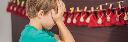 BANNER, LONG FORMAT Smiling boy sitting on a bed opening first present from advent calendar. Winter seasonal tradition. Copy spaceの写真素材