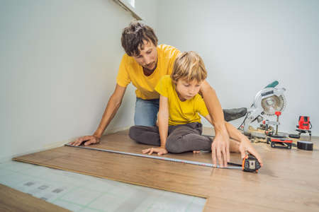Father and son installing new wooden laminate flooring on a warm film floor. Infrared floor heating system under laminate floorの写真素材