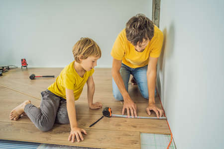 Father and son installing new wooden laminate flooring on a warm film floor. Infrared floor heating system under laminate floorの写真素材
