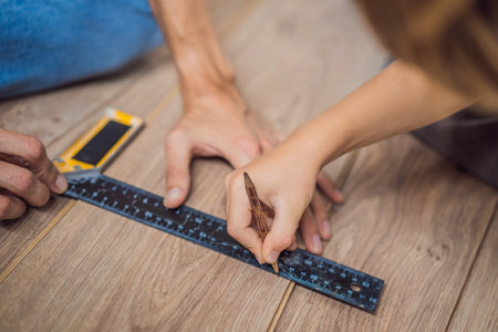Father and son installing new wooden laminate flooring on a warm film floor. Infrared floor heating system under laminate floorの写真素材