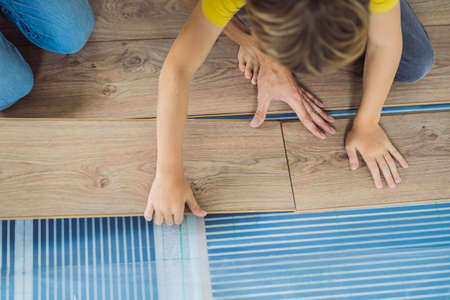 Father and son installing new wooden laminate flooring on a warm film floor. Infrared floor heating system under laminate floorの写真素材