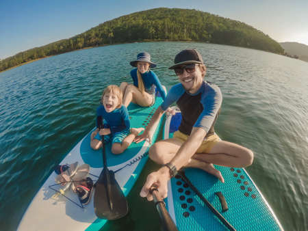 happy family of three, dad, mom and son, enjoying stand up paddling during summer vacationの写真素材