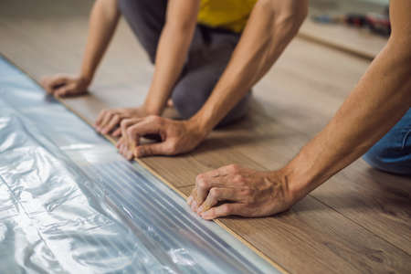 Father and son installing new wooden laminate flooring on a warm film floor. Infrared floor heating system under laminate floorの写真素材