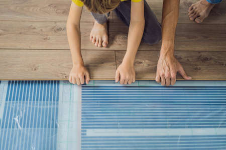 Father and son installing new wooden laminate flooring on a warm film floor. Infrared floor heating system under laminate floorの写真素材