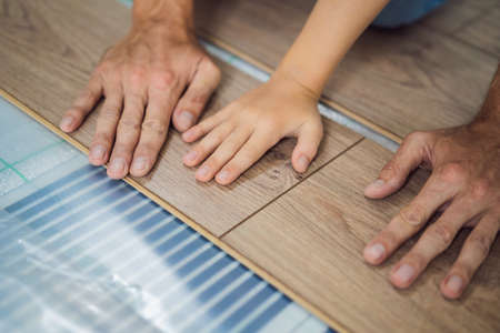 Father and son installing new wooden laminate flooring on a warm film floor. Infrared floor heating system under laminate floorの写真素材