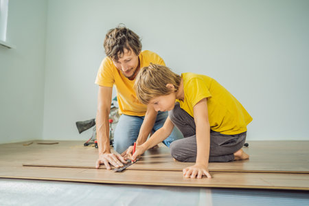 Father and son installing new wooden laminate flooring on a warm film floor. Infrared floor heating system under laminate floorの写真素材
