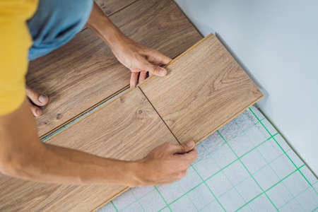Man installing new wooden laminate flooring on a warm film floor. Infrared floor heating system under laminate floorの写真素材