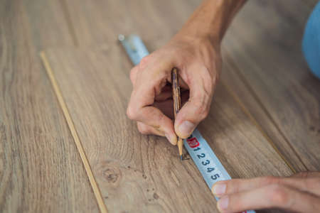 Man installing new wooden laminate flooring on a warm film floor. Infrared floor heating system under laminate floorの写真素材
