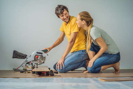 Married couple installing new wooden laminate flooring on a warm film floor. Infrared floor heating system under laminate floorの写真素材