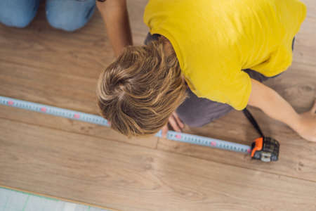 Father and son installing new wooden laminate flooring on a warm film floor. Infrared floor heating system under laminate floorの写真素材