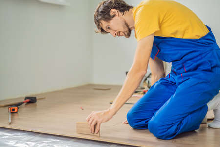 Man installing new wooden laminate flooring on a warm film floor. Infrared floor heating system under laminate floorの写真素材