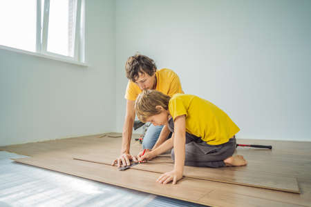 Father and son installing new wooden laminate flooring on a warm film floor. Infrared floor heating system under laminate floorの写真素材