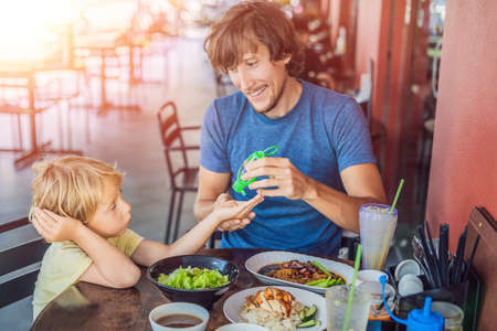 Father and son using wash hand sanitizer gel before eating in a cafe with sunlightの写真素材
