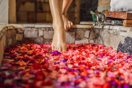 Attractive Young woman in bath with petals of tropical flowers and aroma oils. Spa treatments for skin rejuvenation. Alluring woman in Spa salon. Girl relaxing in bathtub with flower petals. Luxury spa and skin care.の写真素材