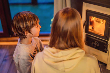 Mom and son spend time by the fireplace in Glamping. Rest in the mountains in Glamping. Cozy fireplace in a mountain houseの写真素材