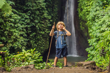 Boy with a trekking stick on the background of Leke Leke waterfall in Bali island Indonesia. Traveling with children conceptの写真素材