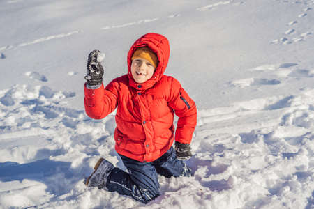 Funny little boy in blue winter clothes walks during a snowfall. Outdoors winter activities for kids. Cute child wearing a warm hat low over his eyes catching snowflakes with his tongueの写真素材